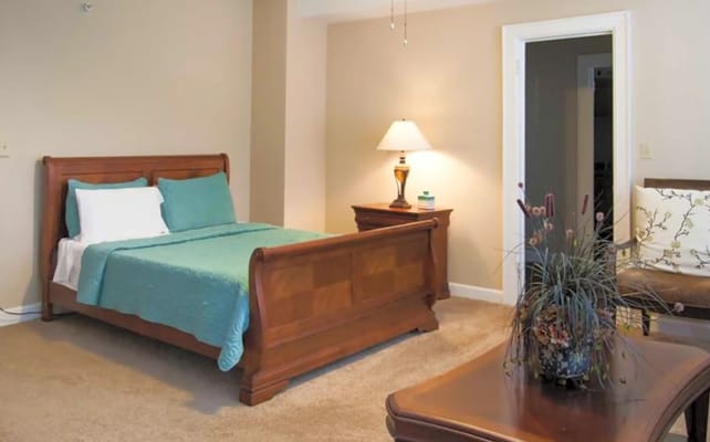 A well-furnished bedroom with a wooden bed, lamp, and armchair.