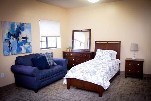 A bedroom with a bed, sofa, and dresser in warm colors.