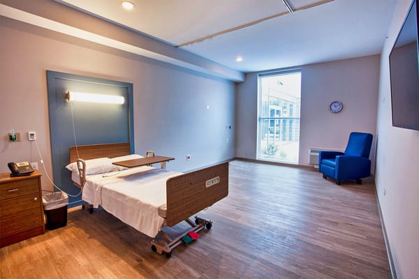Bright and spacious private room with a hospital bed and a chair