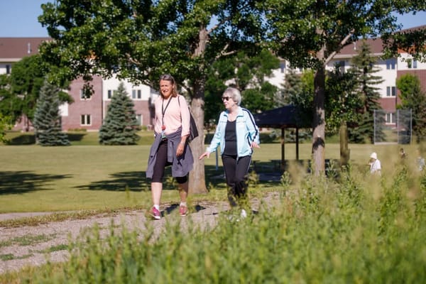Two women walking on a path in a green outdoor space