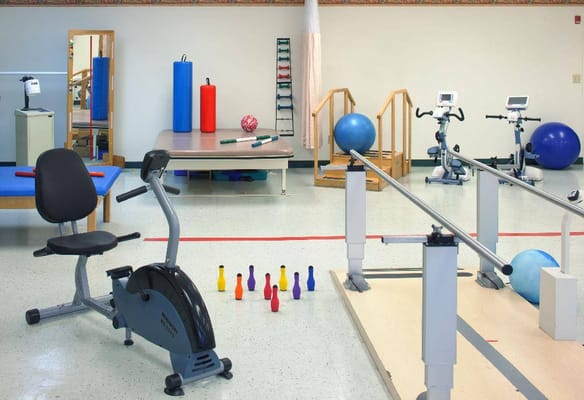 Equipment in the therapy room including exercise bikes, weights, and balance bars.