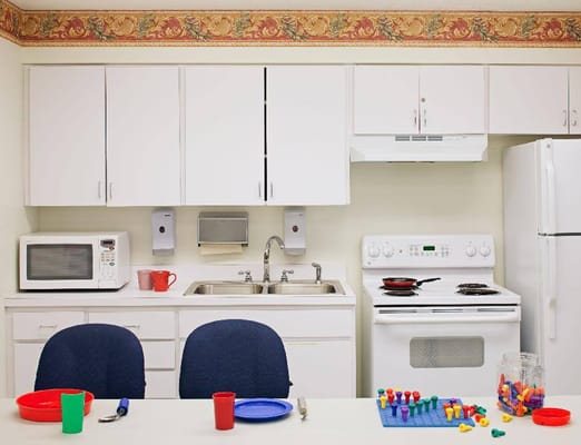 Bright kitchen area with white cabinets, appliances, and a table set for activities