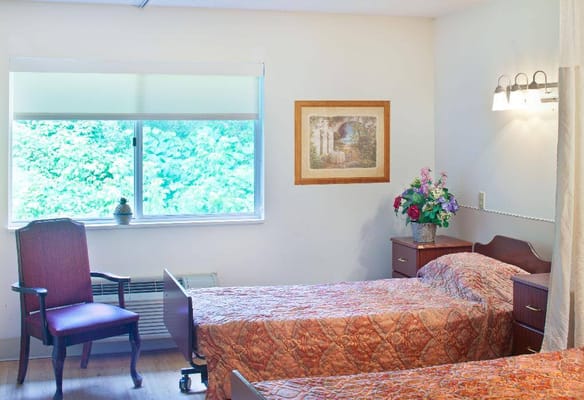 A cozy shared bedroom with two beds, an armchair, and a window overlooking greenery.