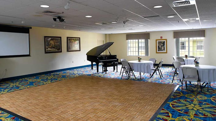 An interior view of a common area with a piano and round tables