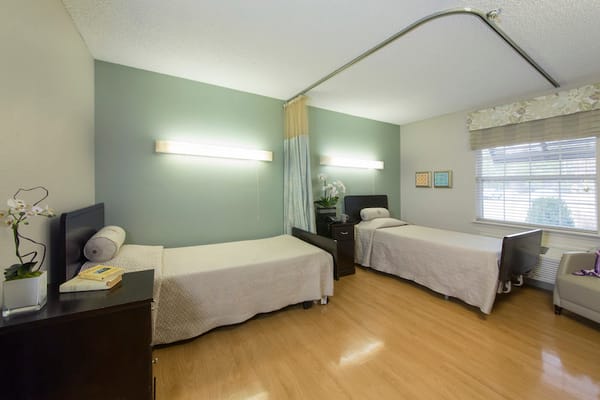 A shared bedroom with two beds, a nightstand, and natural light from a window.
