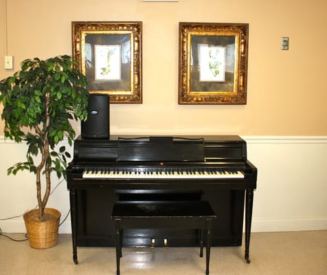 A black piano next to framed artwork on a wall