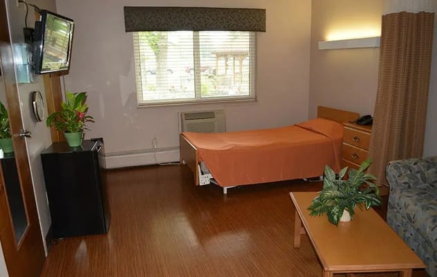 Interior view of a resident room with an orange bedspread, TV, and window.