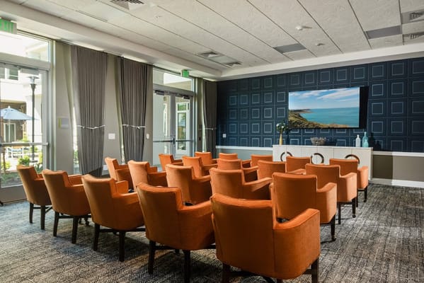 Seating area in the theater room with orange chairs and a large screen