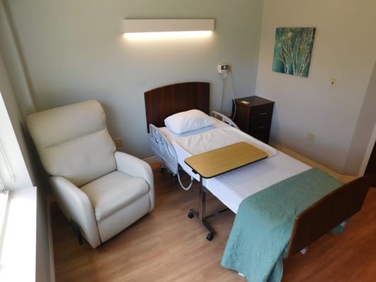 A well-furnished bedroom with a bed, recliner, and bedside table.
