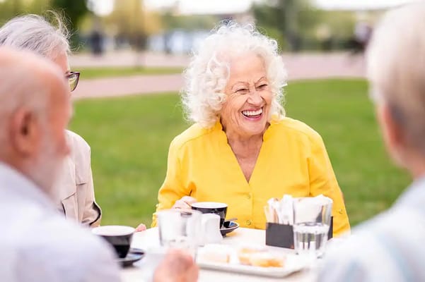 Smiling elderly woman enjoying coffee outdoors with friends