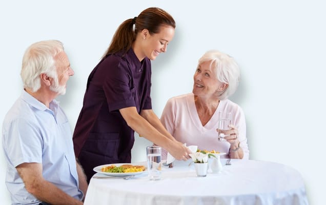 Staff member serving food to residents at a dining table