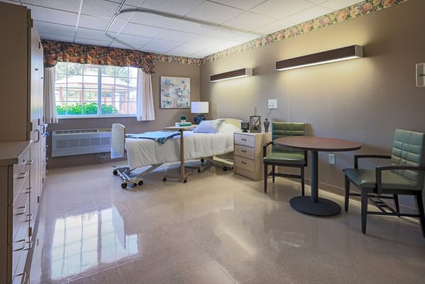 Bright resident room with bed, chairs, and window