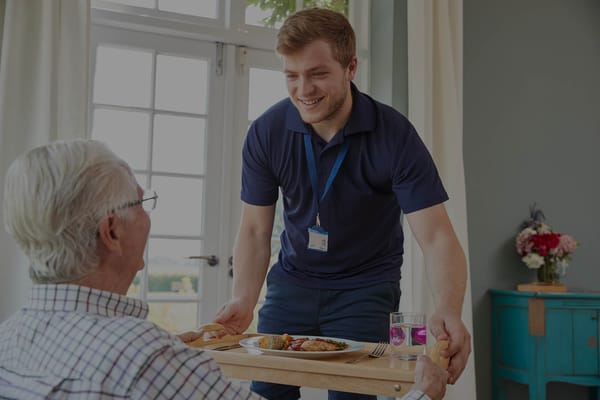 Staff member serving meal to a resident in a cozy interior