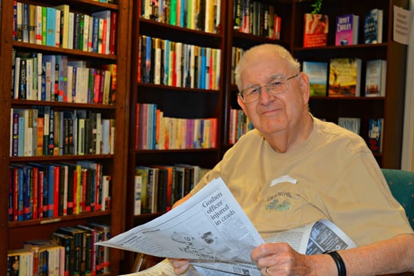 An elderly man reading a newspaper in a library.