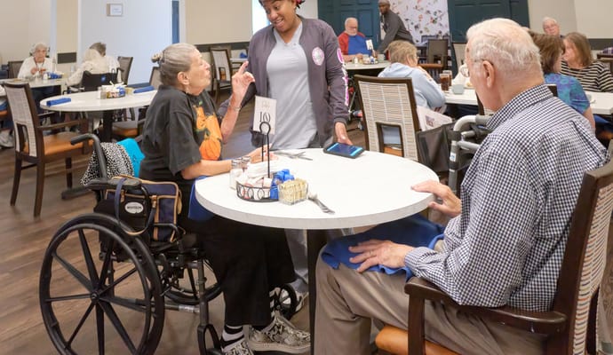 Residents enjoying a meal in the dining room with staff interaction