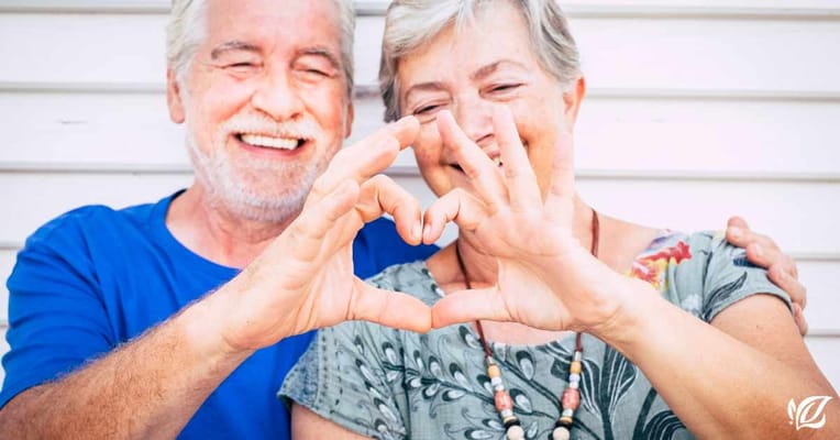 Two smiling seniors forming a heart shape with their hands