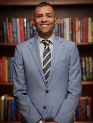 A smiling staff member in a suit standing in front of bookshelves