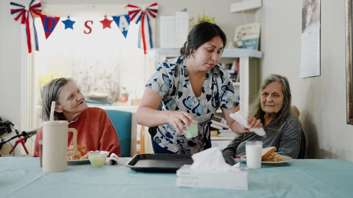 Staff serving food to two residents in a dining area