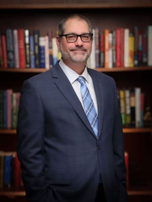 A man in a suit standing in front of a bookshelf