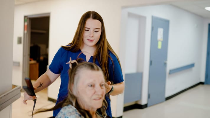 A staff member styling a resident's hair in a hallway