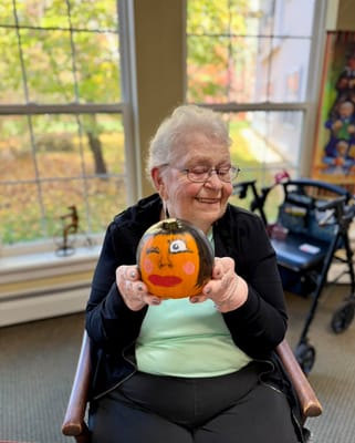 Resident holds a painted pumpkin in an activity room