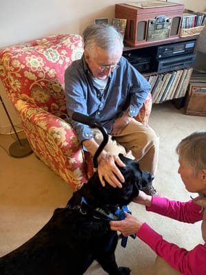 A resident interacting with a dog and staff member indoors