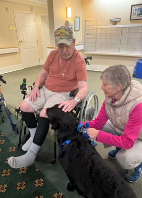 A resident interacting with a dog and staff member in the common area