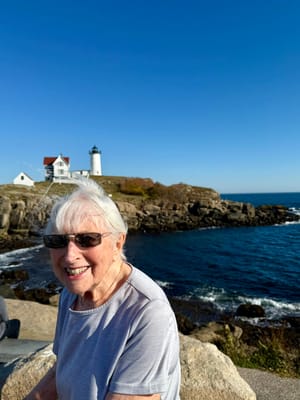 An elderly woman smiling at a seaside lighthouse
