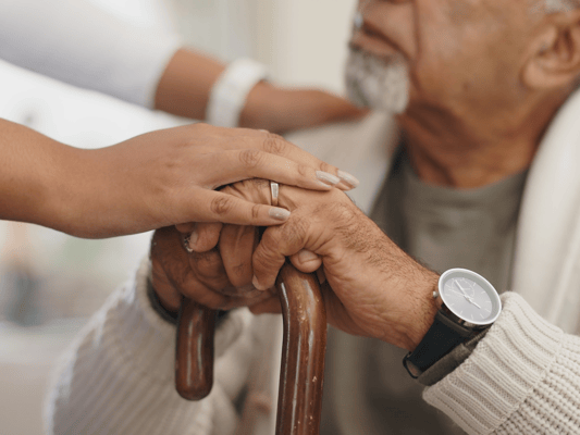 A caregiver's hand holding an elderly man's hand
