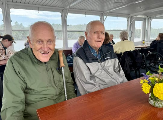 Two elderly men smiling at a table on a boat.