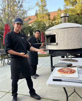 Two staff members presenting a pizza outdoors