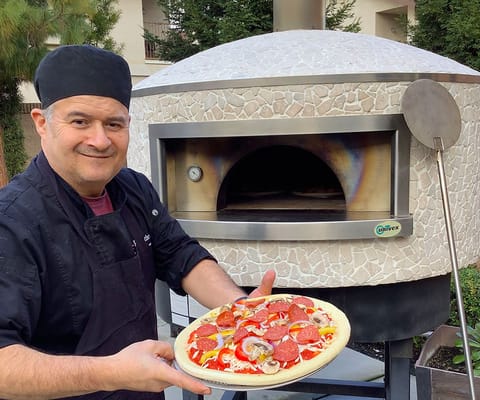 Chef presenting freshly made pizza near outdoor pizza oven