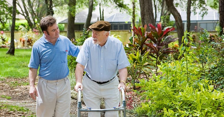 Staff aiding a resident with a walker in a garden
