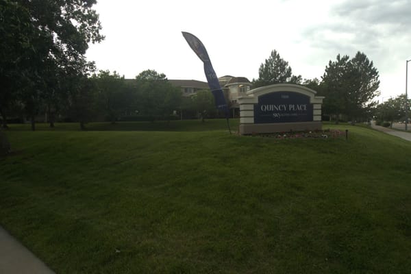 Exterior sign for Quincy Place with a flag and greenery