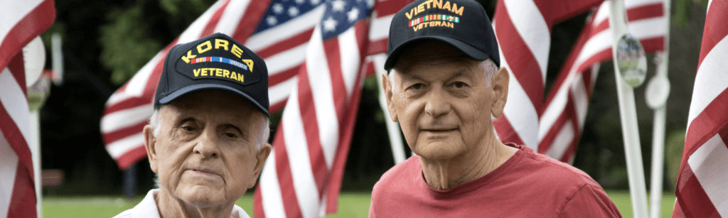 Two veterans in hats standing among flags
