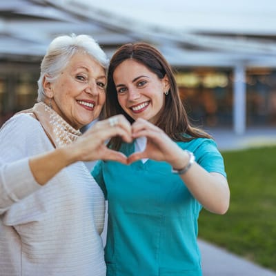 Senior resident and staff member forming a heart with their hands