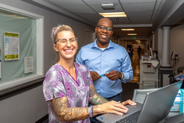 Staff members smiling in a hallway with a laptop