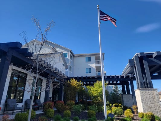 Exterior of Revel Rancharrah senior living facility with landscaped garden and American flag.
