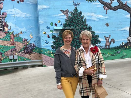 Two women smiling in front of a colorful mural