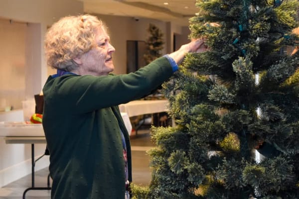 A resident decorating a Christmas tree in a common area