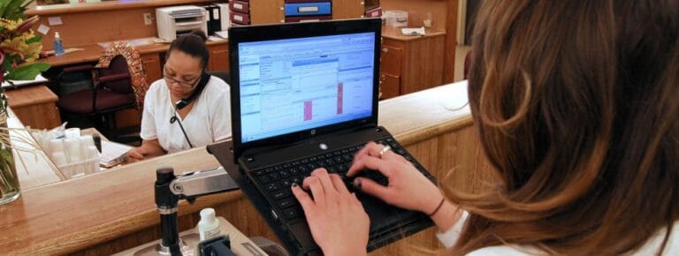 Staff member assisting at the front desk with a laptop