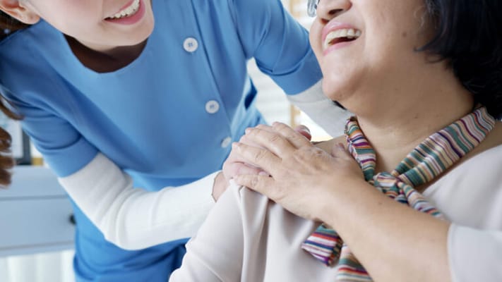 Staff assisting a smiling resident in a bright room