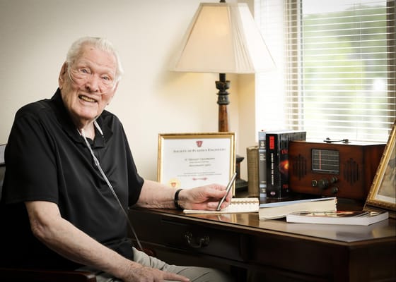 Senior resident sitting at desk with framed certificates