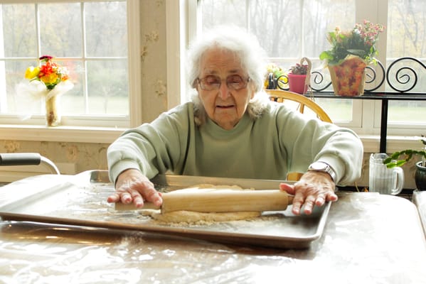 An elderly woman rolling dough in a bright kitchen