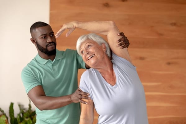Staff assisting an elderly resident with stretching exercises