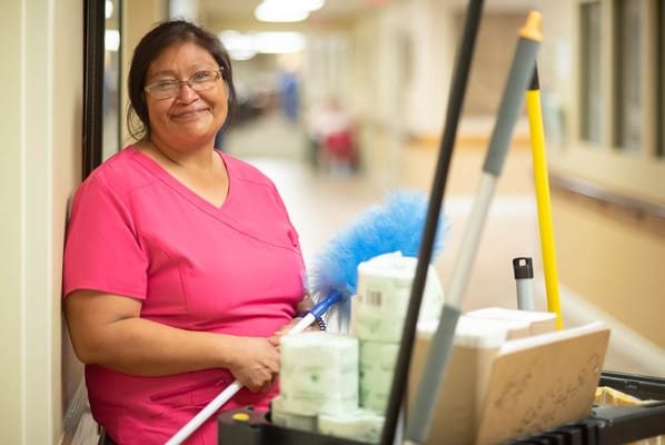 Staff member smiling in a corridor with cleaning supplies