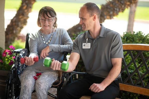 Therapist assisting resident with weight exercises outside