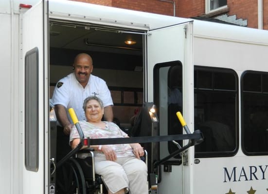 Caregiver assisting a resident in a wheelchair from a vehicle