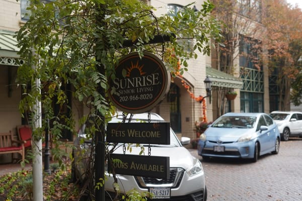 Sign displaying 'Sunrise Senior Living' and welcoming messages surrounded by greenery.