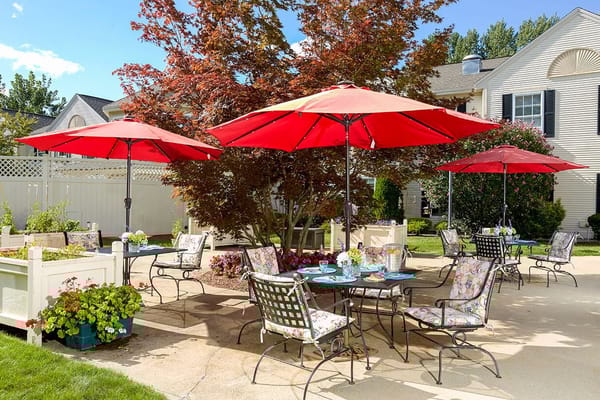 Outdoor patio with tables under red umbrellas and floral arrangements.